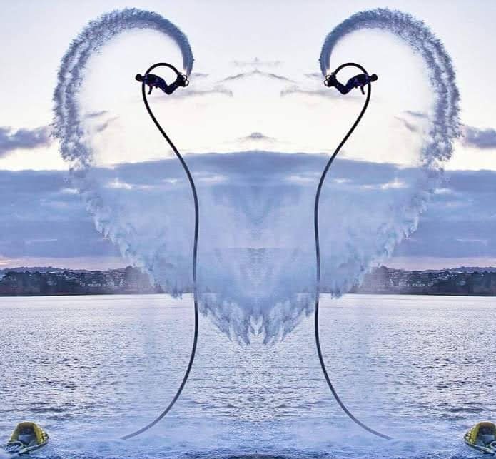Two flyboarders drawing a heart of spray over a calm bay