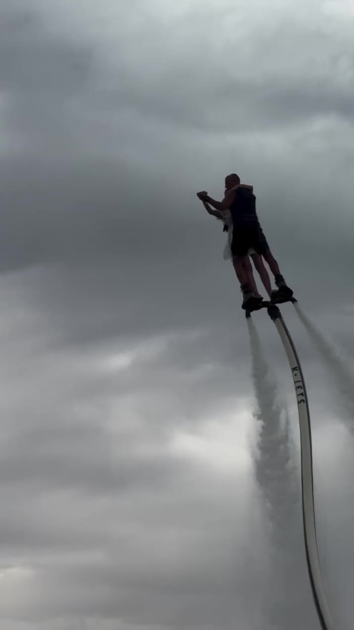 Couple in a white dress flying tandem on a flyboard against a storm sky