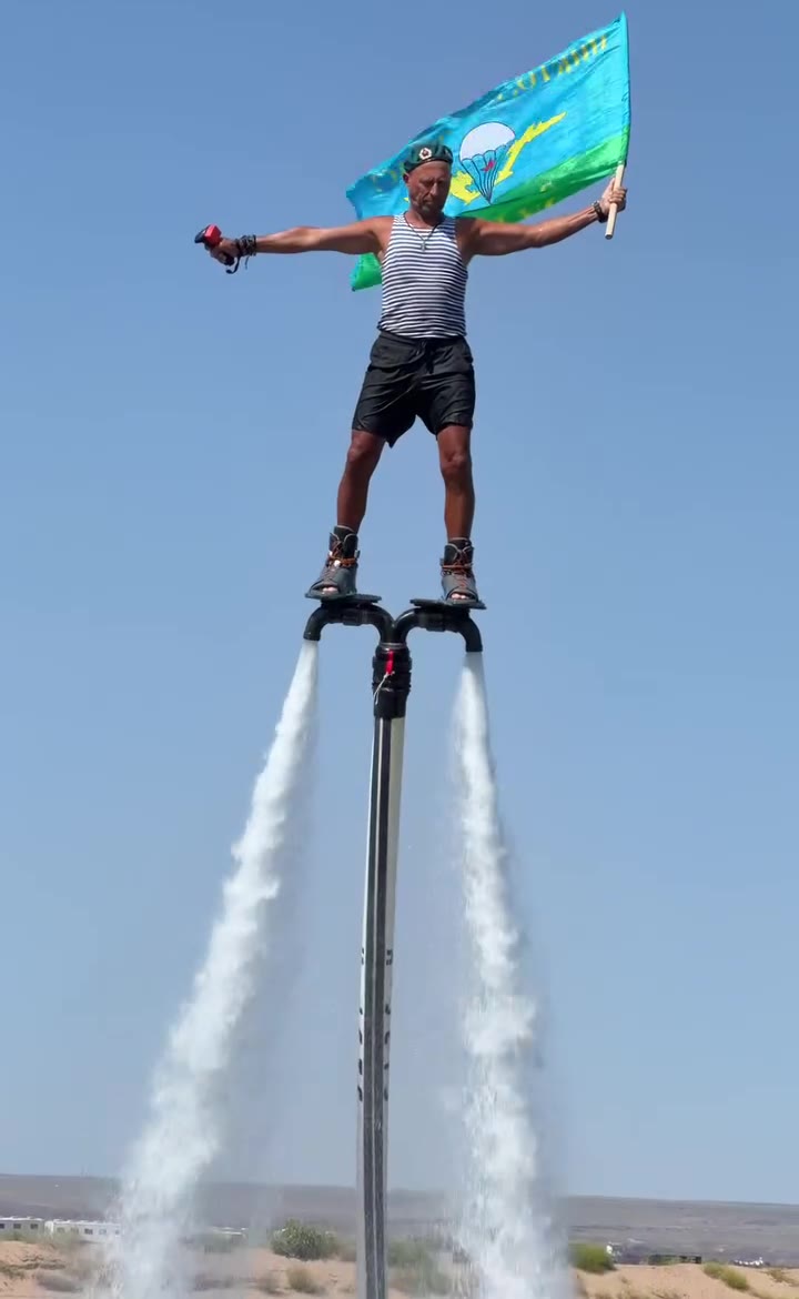 Valerii Super Pilot Pro on a flyboard against blue sky, flag in one hand, throttle in the other