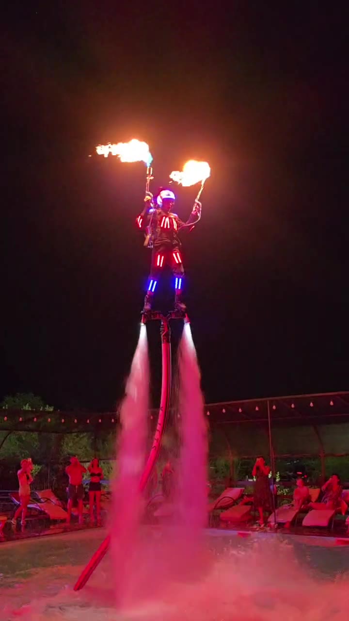 Night flyboard show in a hotel pool: LED suit, dual fire torches, and spark wings over the water